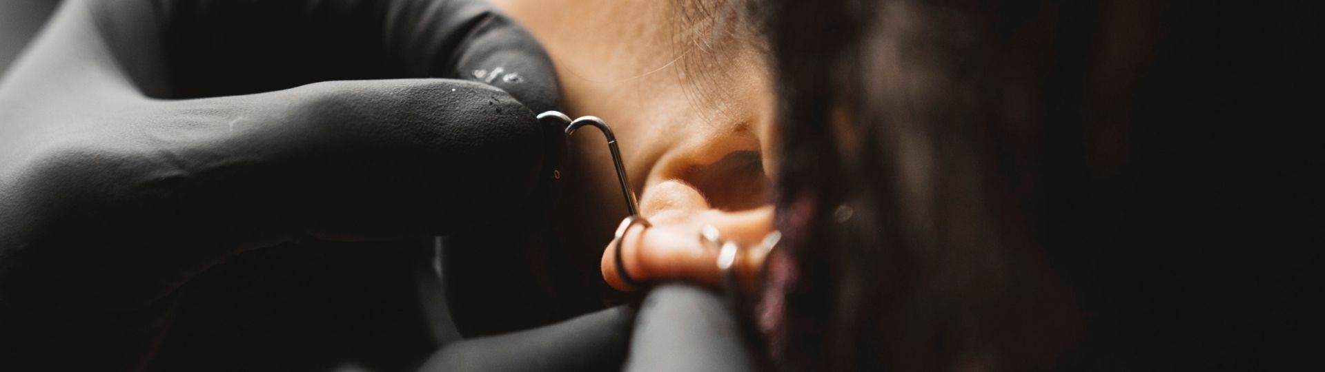 Piercer nasazuje titanovou piercingovou náušnici klientce do ucha v piercingovém studiu CryptoCrew